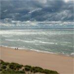 Two people walk the beach along Lake Michigan.